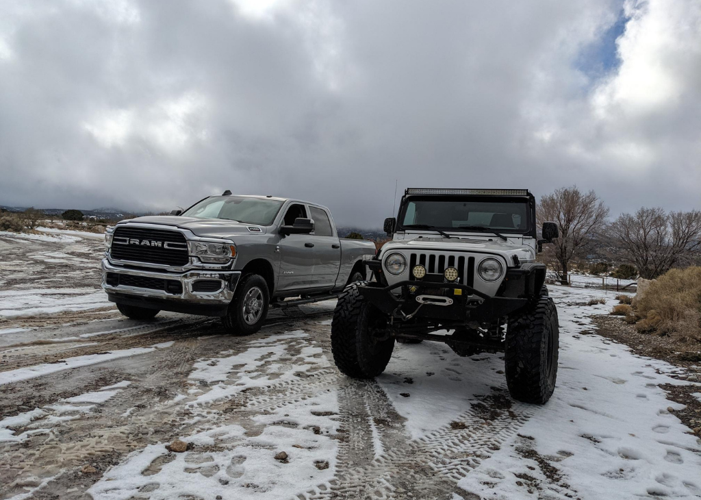 A silver jeep and truck on the slightly snowy trail and it's a cloudy day