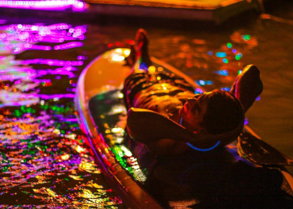 Man laying down on paddle board with neon glow over the water at Lake Las Vegas in Henderson