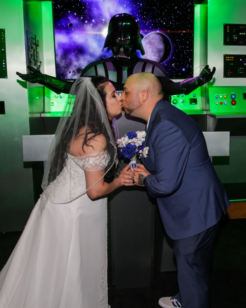 A couple kissing Darth Vader presiding over ceremony