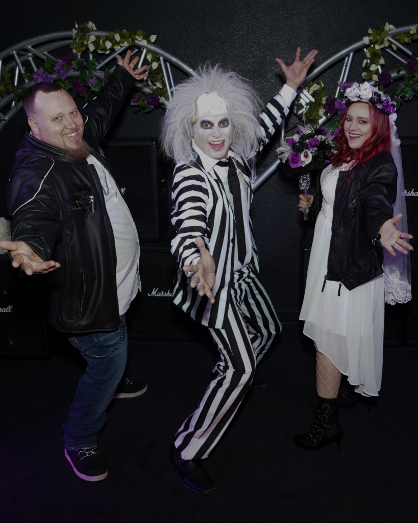 A wedding couple in between Beetlejuice impersonator officiant