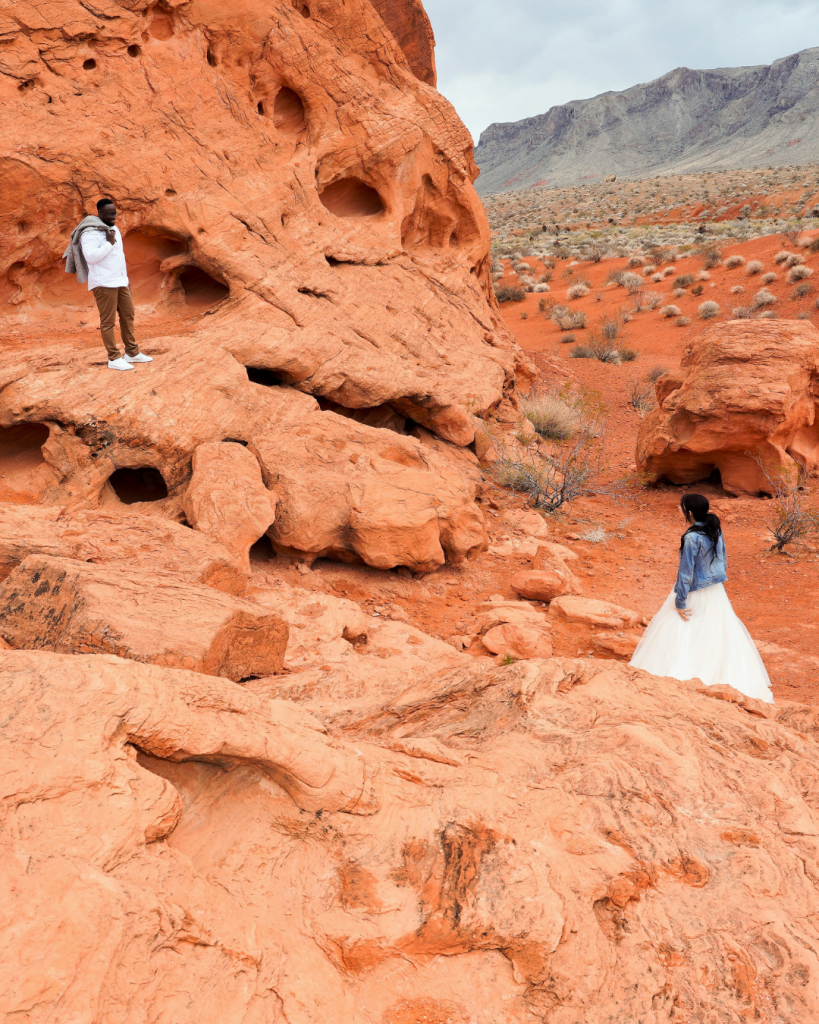 Groom on a rock at valley of fire starring down at bride rocks are beautiful orange sunny day
