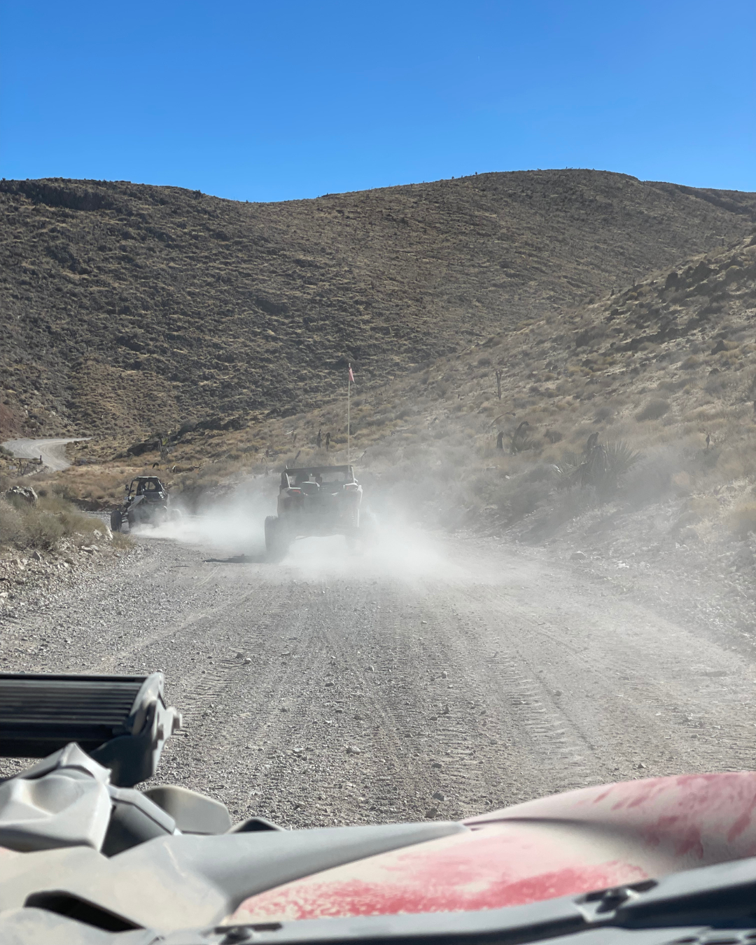 A view from a UTV looking at two UTVs kicking up dust at Adrenaline Mountain in Goodsprings