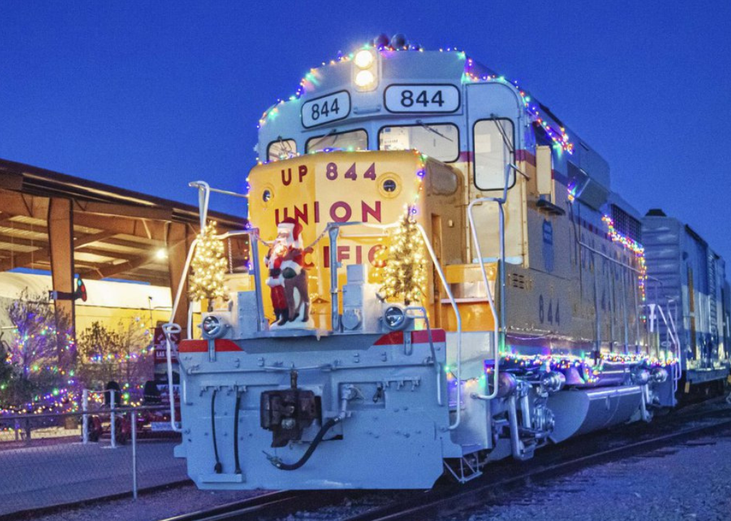 A train with holiday lights and a Santa figurine on the conductor platform.