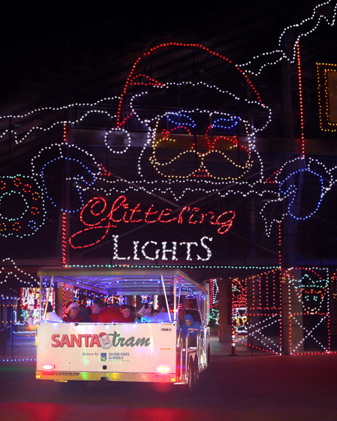 A tram with people drive through a giant santa head in lights as they enter the first tunnel of lights at Glittering Lights