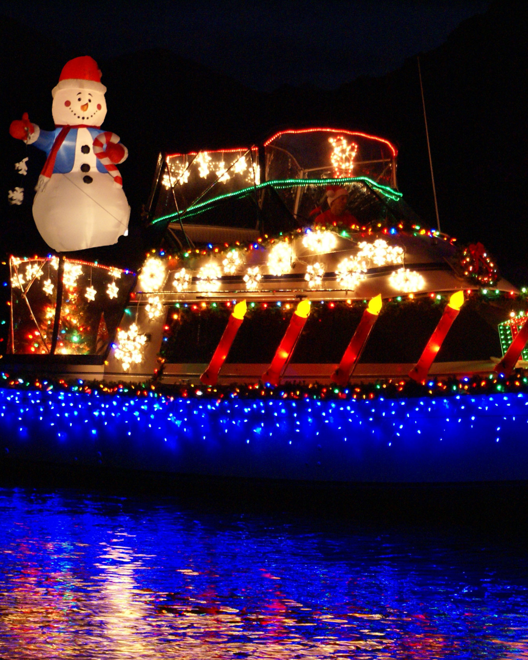 A boat with holiday lights and snowman waving.