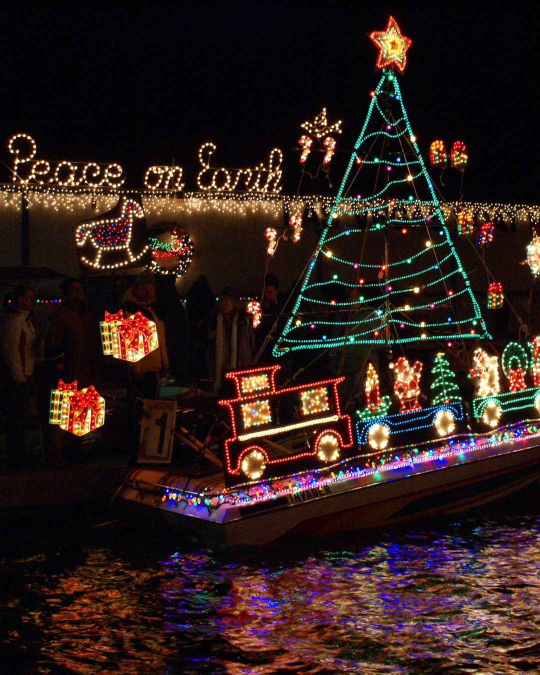A boat decorated with a christmas tree, train and in lights it says Peace on Earth.