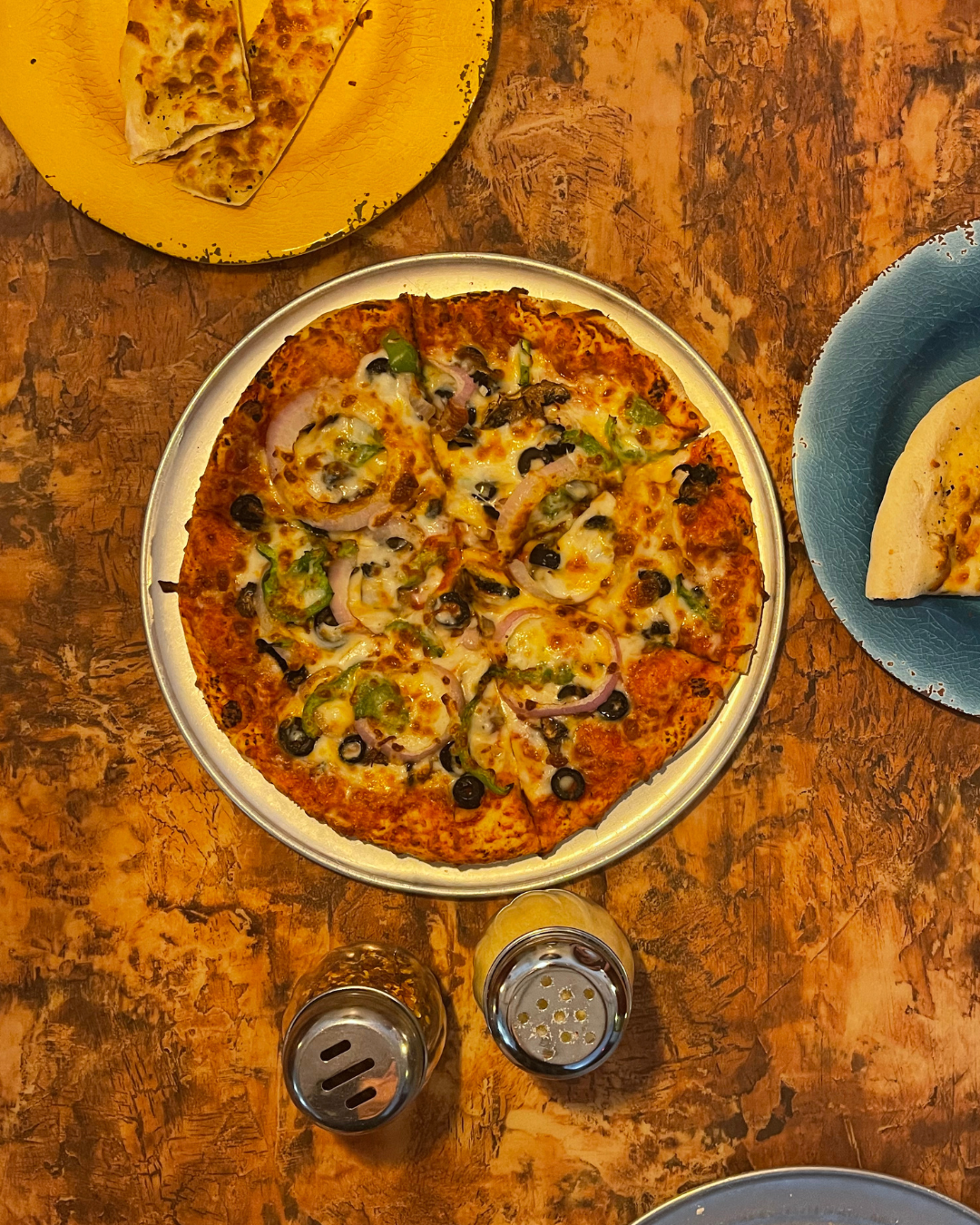 A table at pirates landing with a veggie pizza, red flakes and parmesan shakers