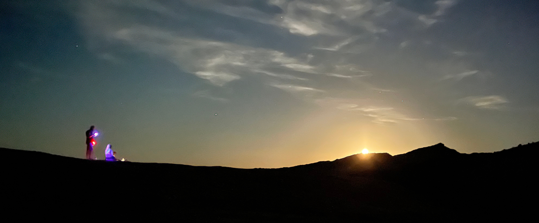 Two people on the Fire Wave Trail Rocks watching the moon crest over the Valley of Fire.