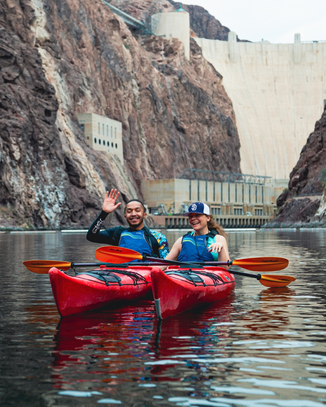 A man and woman in red kayak's taking a tour with a view of Hoover Dam in the background