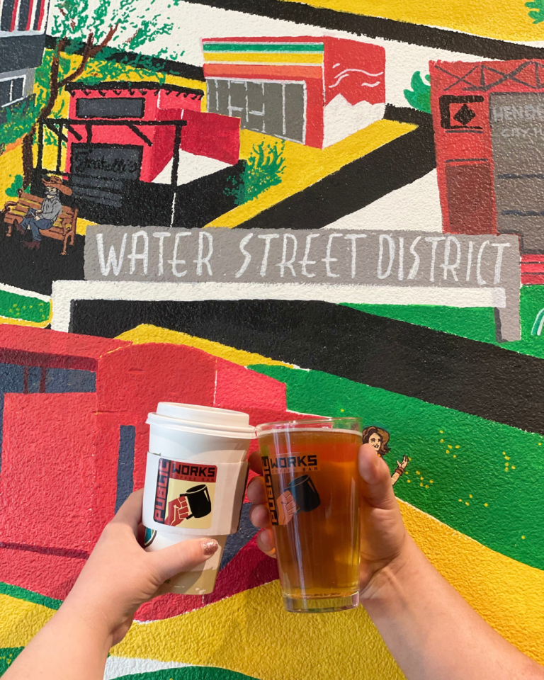 White coffee cup and beer cheers against a colorful mural of water street district