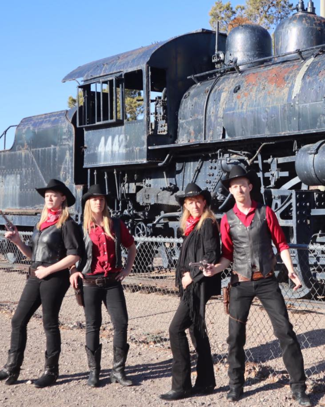 Mama's Wranglers three females one mail dressed in red shirts and black leather in from of a steam train.