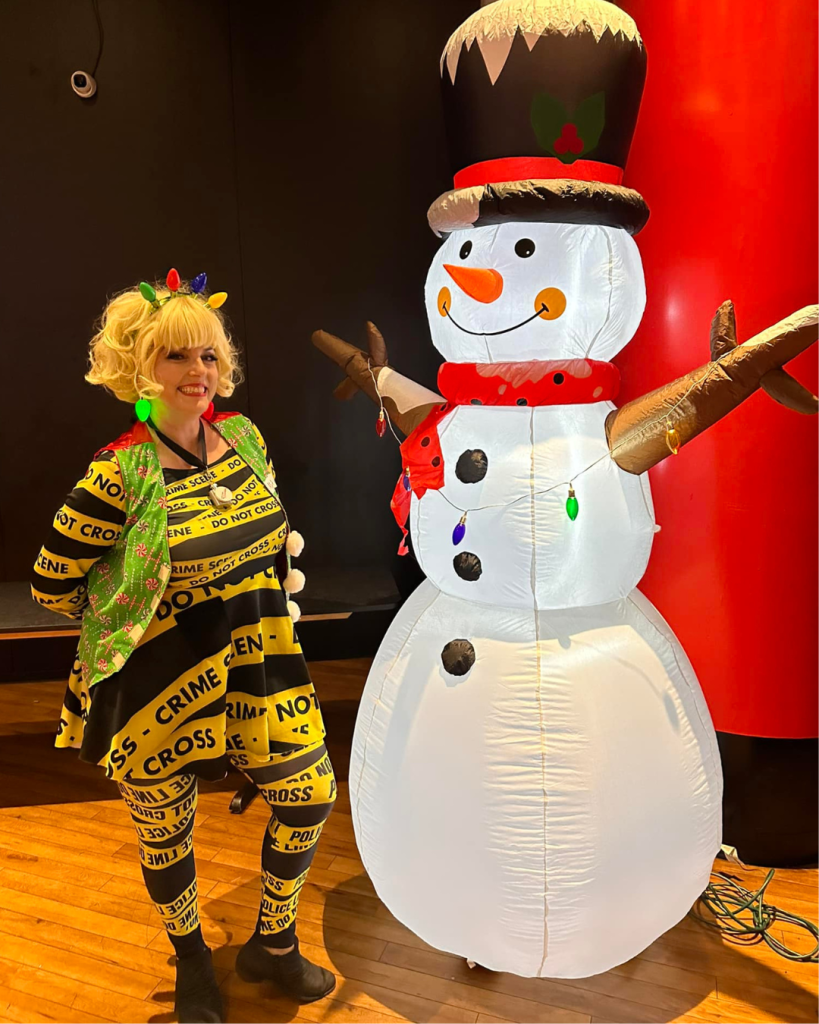 Marriage Can Be Murder's ditzy hostess gets merry decked out in a headband with lights standing next to an inflatable snowman.