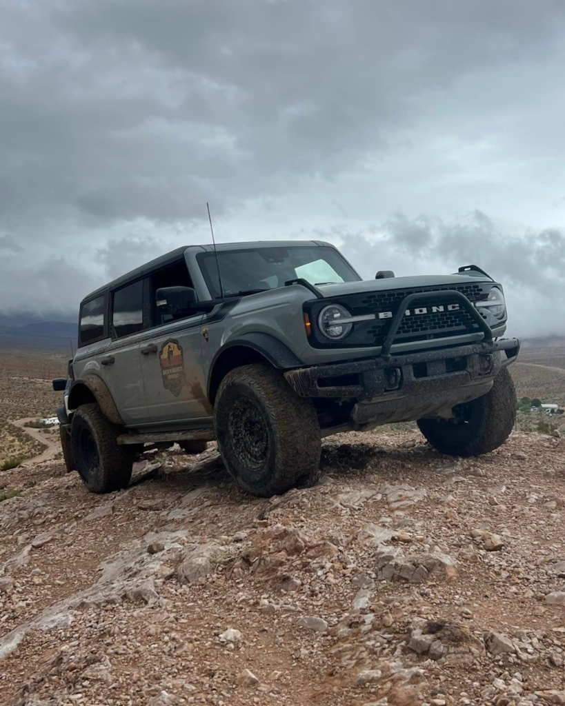 A very cloudy overcast sky with a bronco on top a very hilly terrain.