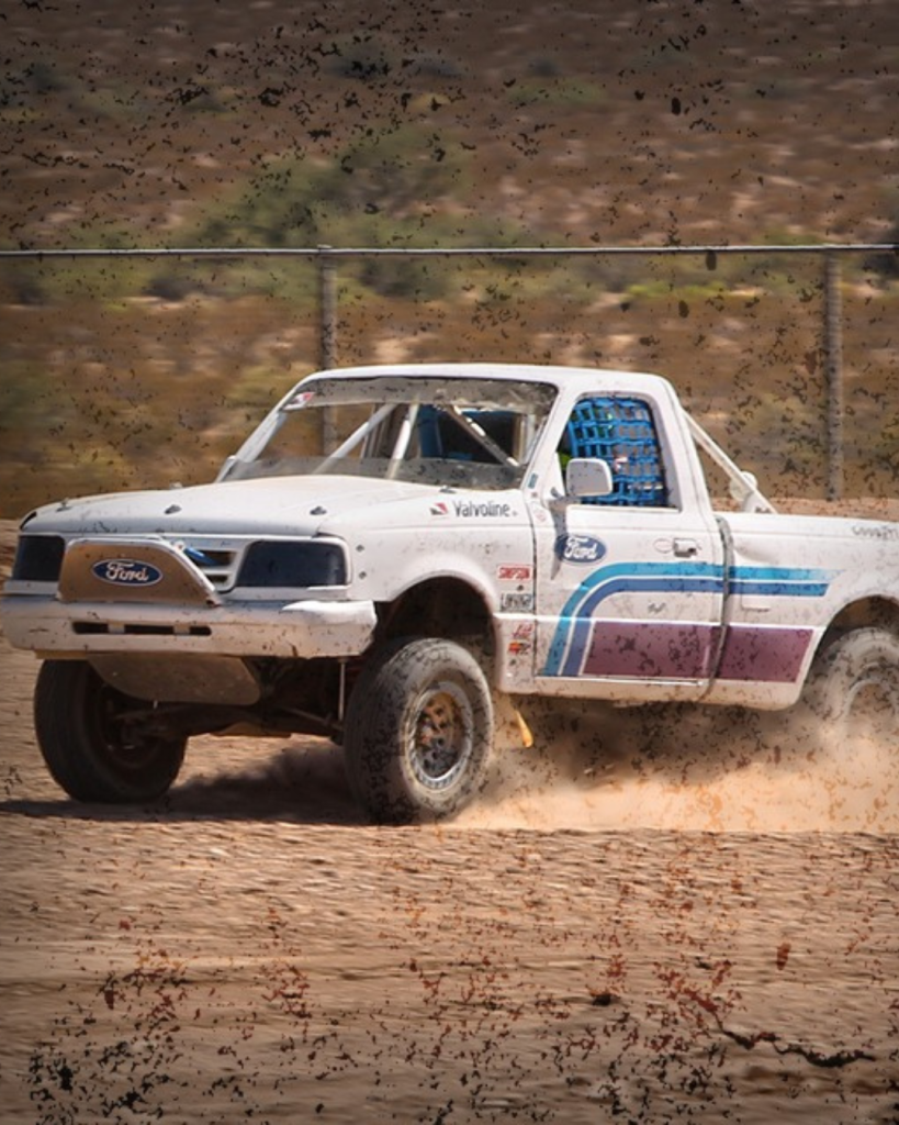 A white ford with purple and blue stripes ripping through a desert track at a fast paced roll. Tour company: Las Vegas Outdoor Adventures