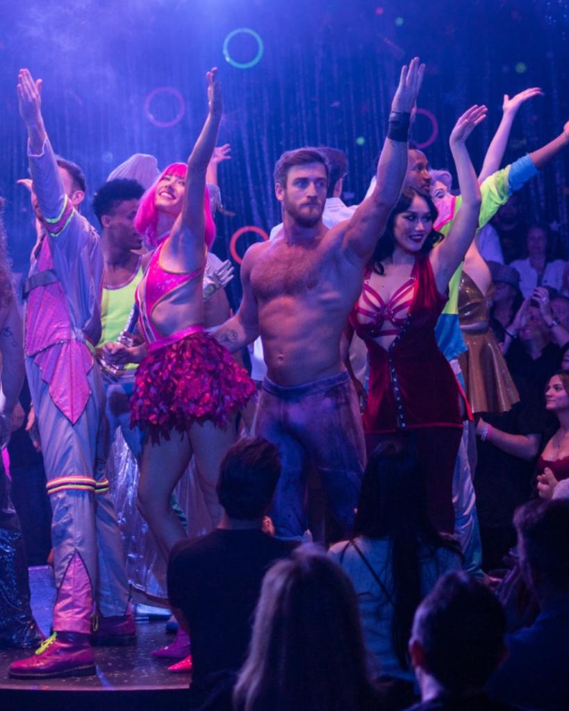 OMP performers on stage at the end of the show with arms in the air.