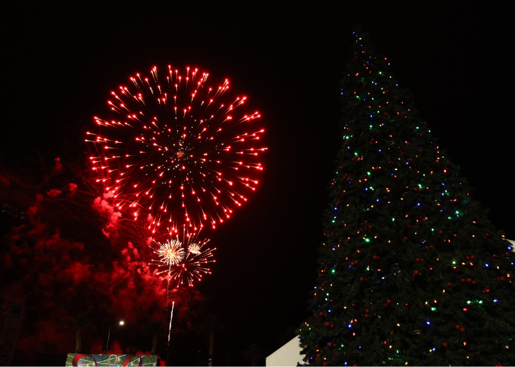 Red fireworks next to a giant christmas tree.