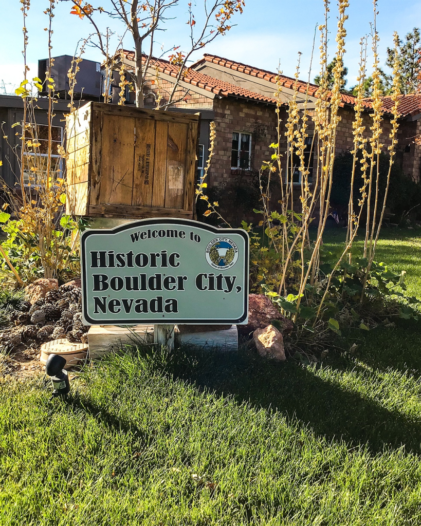 Boulder City sign on green grass says welcome to historic Boulder City. Photo courtesy of National Park Express