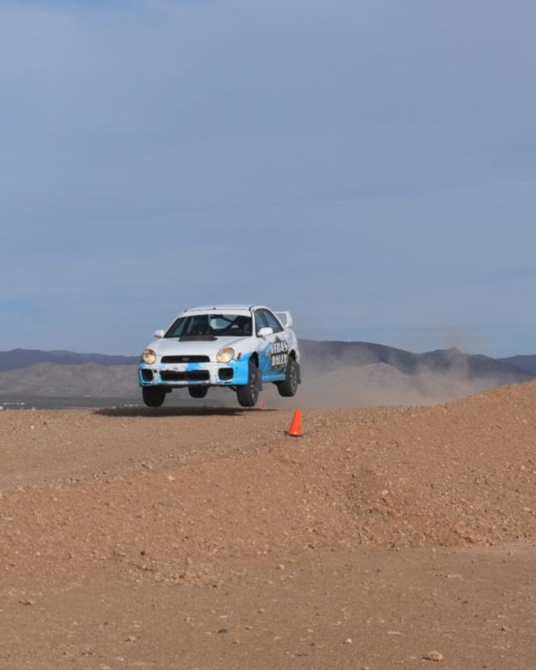Las Vegas Outdoor Tours off-road experience a racing car is up off the ground as it speeds through the dirt track in the desert on a hazy day.