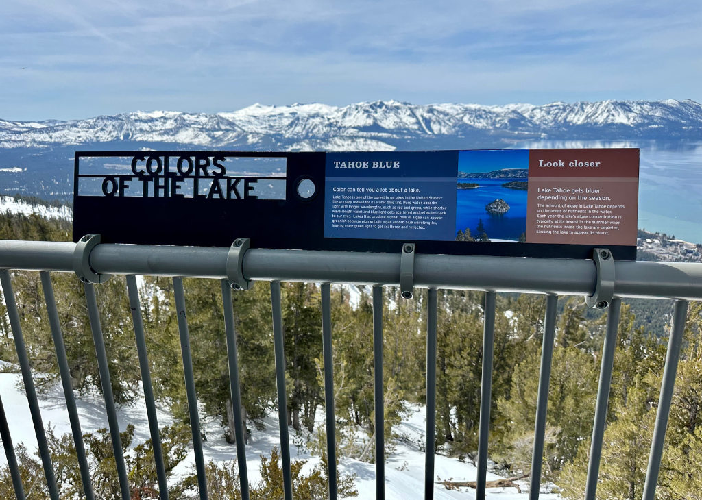 A view of Lake Tahoe and its surrounding mountains from the Nevada side at Heavenly Mountain Resort. There is a sign that talks about the colors of the lake.