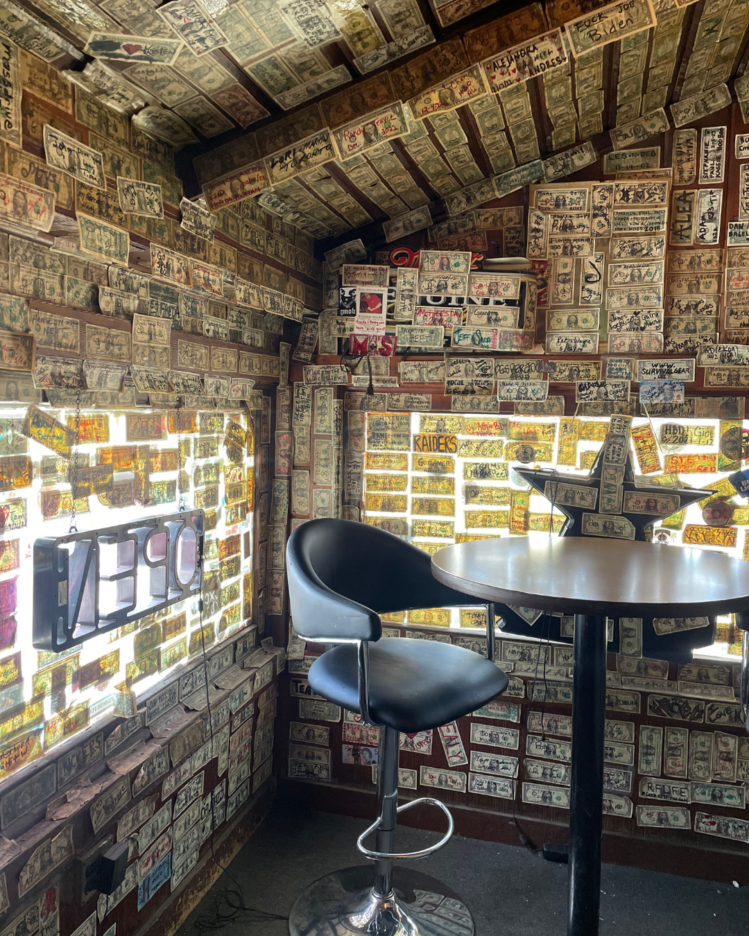 A bar table at Mountain Springs Saloon and the windows and walls are covered with american bills written on. This saloon in on a mountainside has outdoor concerts, grub and home to many bikers cruising around exploring Nevada.