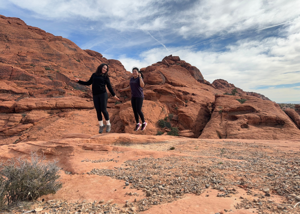 Two girls jumping on a hiking trail with red rocks and blue sky day at Red Rock Canyon.