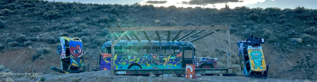 A bus and two cars on a hill with a picnic area at the open-air art gallery called International Car Forest of the Last church outside of Goldfield.