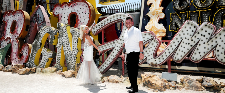 A couple in wedding clothes posing in front of old neon signs in the Neon boneyard at the Neon Museum.