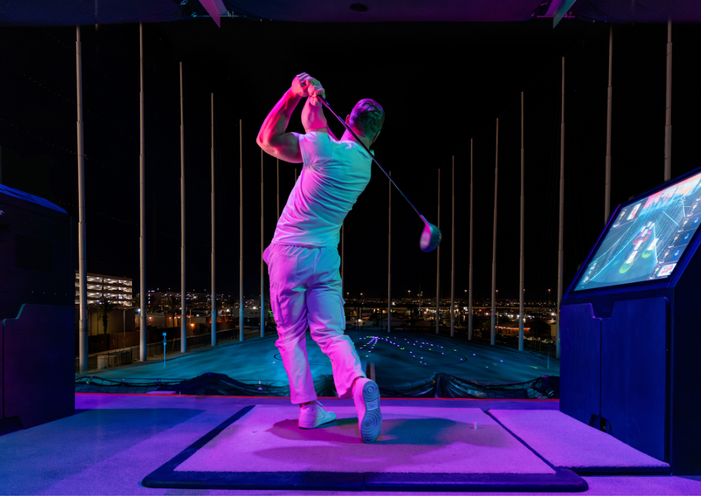 A man swinging at Atomic Golf Las Vegas at night with a purple party vibe glow ing