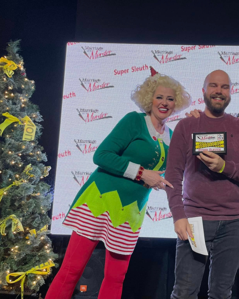 Two people stand by a Christmas tree; a man holds a certificate in Las Vegas Territory.