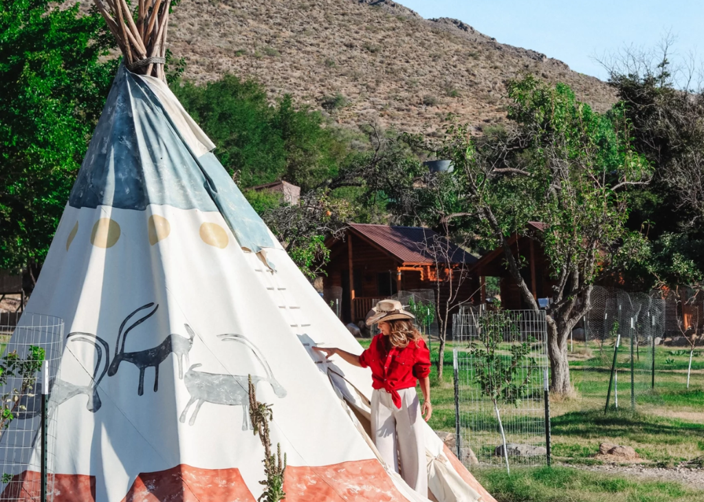 A female in. cowboy hat going into a tipi at Aravada Springs.