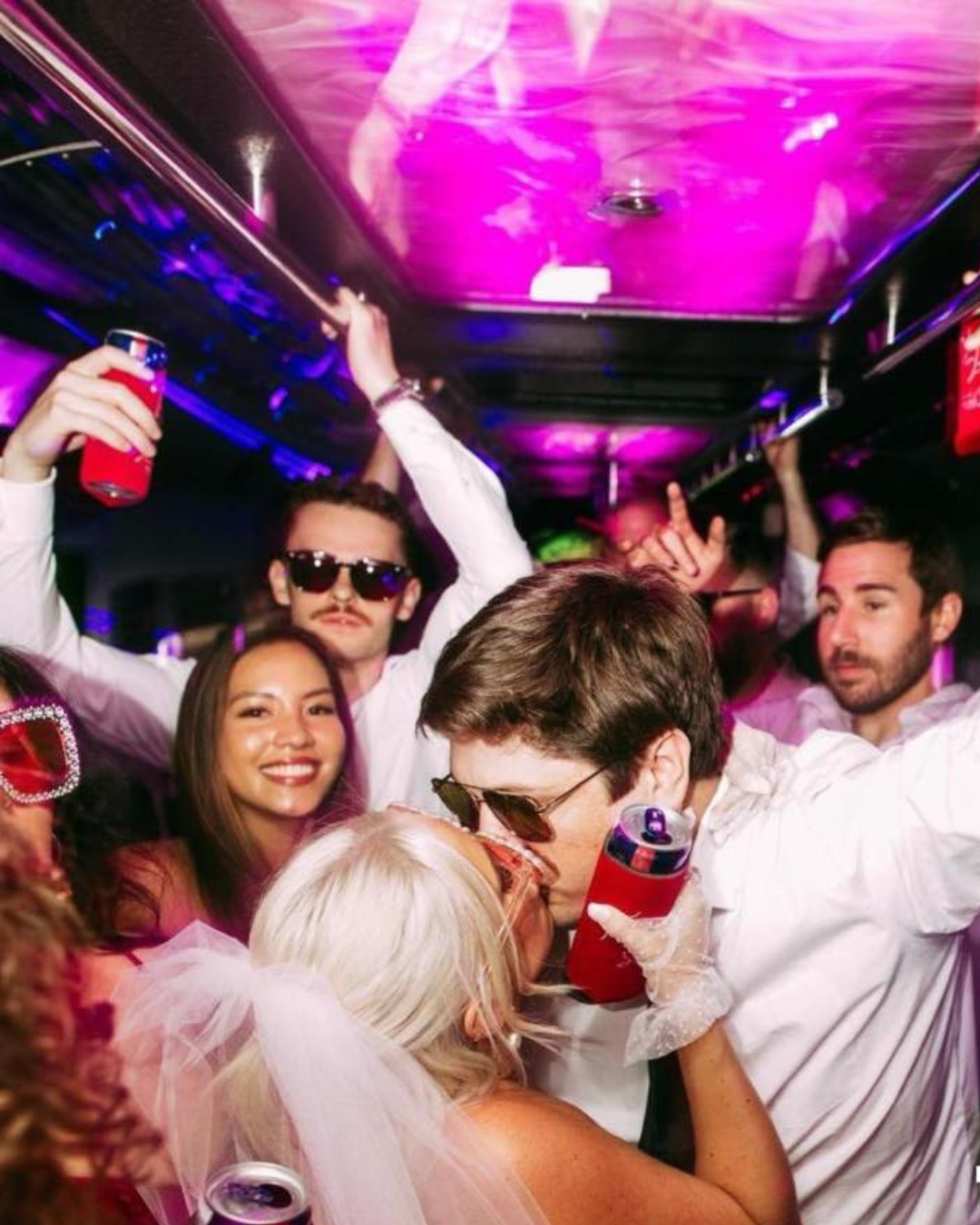 A couple kissing on the Discreet party bus with their surrounded by their wedding party holding koozies and beer.