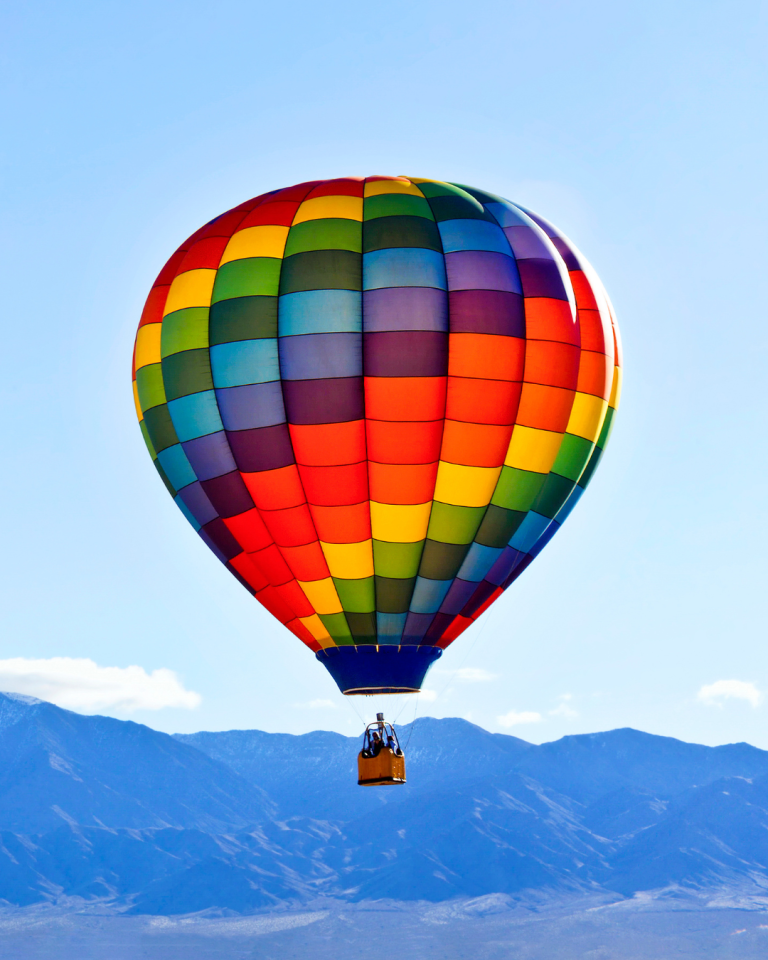 Hot Air Balloon Festival in Mesquite, Nevada. A lone rainbow colored one floating across the blue sky with mountains in the background.