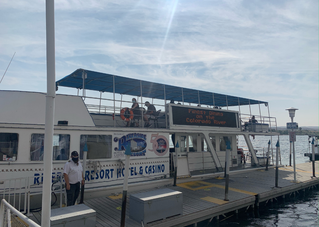 Side of the USS Riverside Cruise boat with drive and people hanging out by the dock